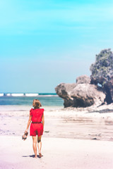 Girl in a red dress walking barefoot on the sea shore. Tropical beach, Bali island. Sunny day.