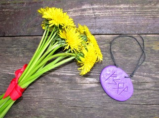A bright yellow bouquet of dandelion flowers, tied with a red ribbon, lies on a wooden bench next...
