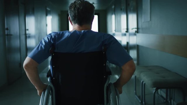 In the Hospital, Front View Following Shot of the Elderly Man in the Wheelchair Moving through the Hallway. Shot on RED EPIC-W 8K Helium Cinema Camera.