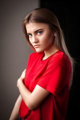 Portrait  serious beautiful young woman in red t-shirt and jeans posing with hands on hip and looking at camera in  studio  on black background