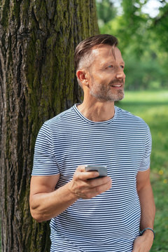 man leaning on a tree trunk holding his mobile phone