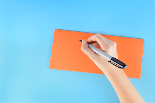 On a blue background lies an orange envelope. The hand of a young girl signs it.