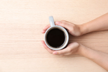 Young woman with cup of delicious hot coffee on wooden background, top view