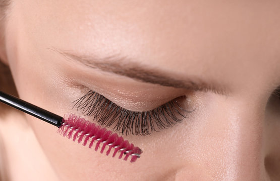 Attractive young woman applying mascara on her eyelashes, closeup