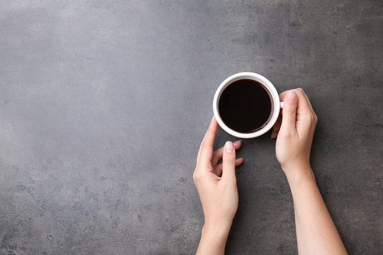 Young woman with cup of delicious hot coffee on grey background, top view