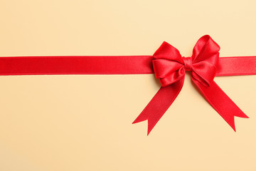 Red ribbon with bow on color background, top view