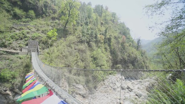 A long metal strong bridge across dry river, route for trek at Annapurna base camp with Colorful Prayer Flags blowing hang on Sign for People to good luck journey 