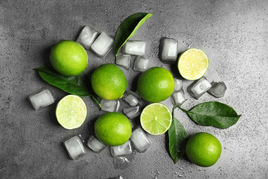 Composition with fresh ripe limes and ice cubes on gray background, top view