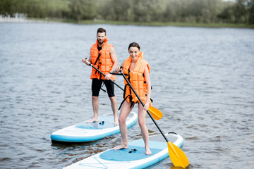 Couple in life vests learning to row on the stand up paddleboard on the lake