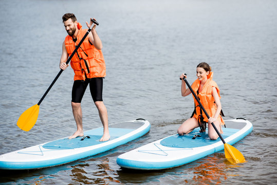 Couple in life vests learning to row on the stand up paddleboard on the lake