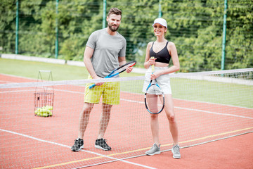 Young couple having fun standing together on the tennis court relaxing after the match outdoors