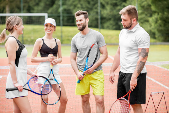 Group of friends having fun standing together with rackets on the tennis court