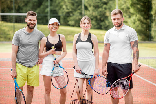 Portrait of a group of young friends in sportswear standing with rackets on the tennis court outdoors