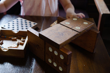 One child is playing a jiant dominoes made of wood and other toys on an old wooden table.