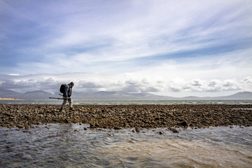 Photographer walking with his tripod and backpack on the beach of Newborough, Wales