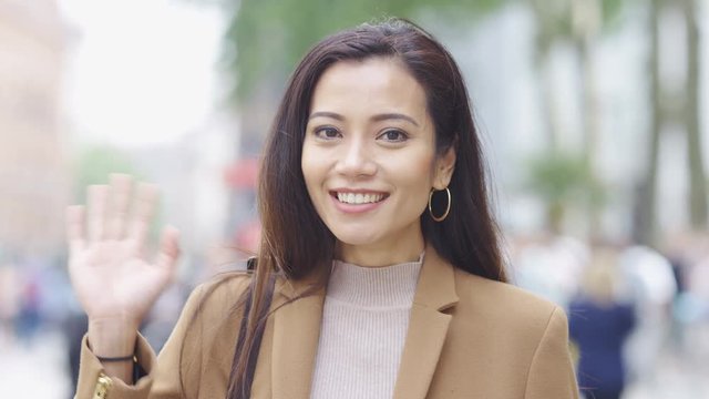 Portrait of smiling asian woman waving to camera, in slow motion