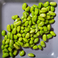 Green fresh soybeans on gray square plate on pink background. Healthy food concept. Top view.
