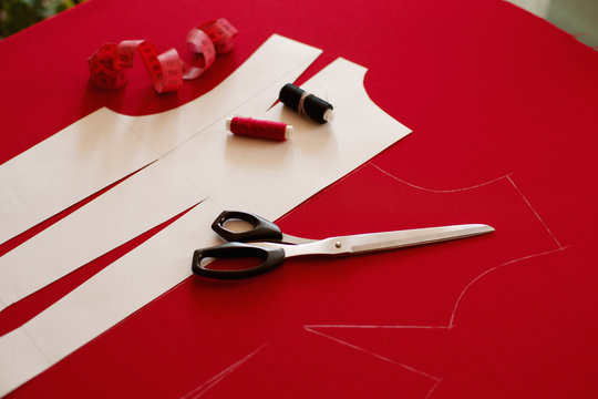 Sew clothes made of red cloth. Paper pattern, tailoring scissors, centimeter tape and thread for sewing clothes. Sewing a dress according to the drawing.
