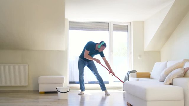 people, housework and housekeeping concept - happy man in headphones with mop cleaning floor and dancing at home