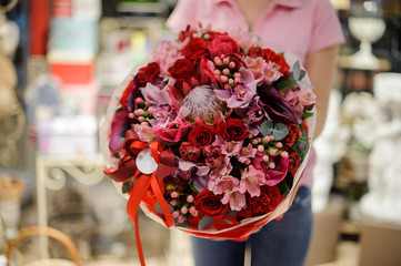 Florist holding a large bright bouquet in red tones consisting of roses and other beautiful flowers