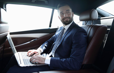 businessman with laptop sitting in the back seat of a car