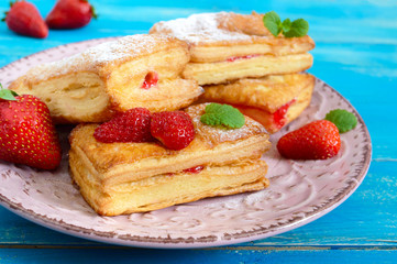 Sweet tasty puff pastry dessert on plate on wooden background. Delicious homemade cookies with strawberry jam, berries and sugar powder.