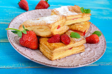 Sweet tasty puff pastry dessert on plate on wooden background. Delicious homemade cookies with strawberry jam, berries and sugar powder.