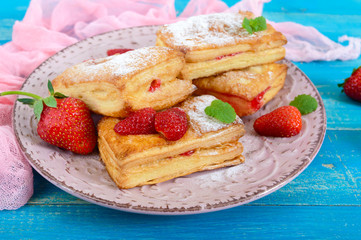 Sweet tasty puff pastry dessert on plate on wooden background. Delicious homemade cookies with strawberry jam, berries and sugar powder.
