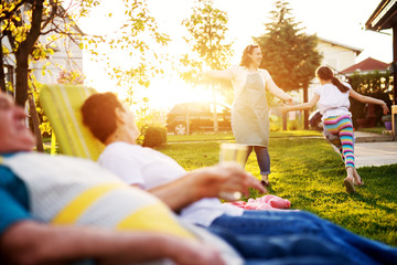 Cheerful woman is playing with her daughter in front of the house on a beautiful day while her...