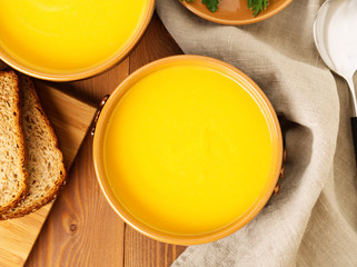 Two brown bowl of pumpkin soup on brown dark wooden background, top view, close up.