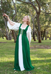 full length portrait of blonde girl wearing greensand white medieval costume, standing pose. walking through a forest. © faestock