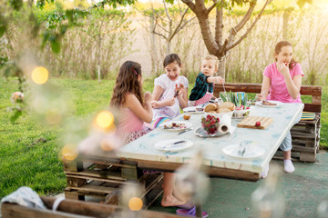 After they finished meat from the stick, two playful girls are poking each other with sticks while their older sister and toddler brother are eating.
