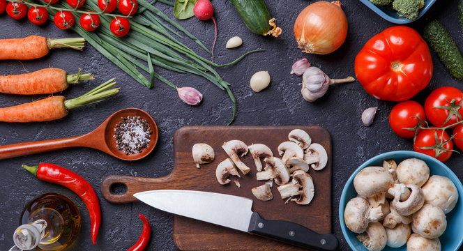 Image on top of fresh vegetables, mushrooms, cutting board, oil, knife