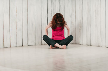 a pretty long-haired girl in a pink top, sitting cross-legged on the floor, head down, light background