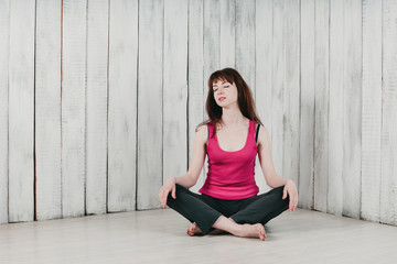 a pretty long-haired girl in a pink top, sitting cross-legged on the floor by the wall, eyes closed, smiling, light background