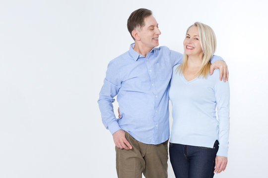 Full Length Portrait Of Happy Mature Couple Standing With Hands In Pockets Over White Background