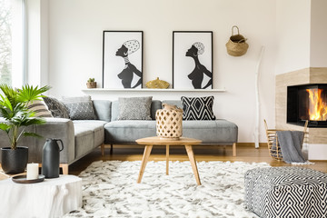 Patterned pouf next to wooden table in african living room interior with posters. Real photo