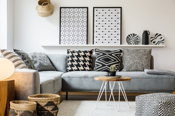 Patterned pillows on grey corner sofa in apartment interior with posters and pouf. Real photo