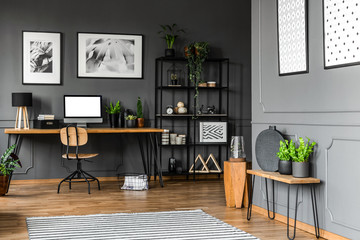 Black rack with decorations standing next to a wooden chair and desk with plants, lamp and a...