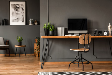 Real photo of an open space interior with black walls and molding. Workspace with desk, chair and...