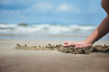 Happy child playing with sand at the beach in summer