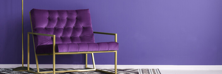 Purple armchair with gold metal frame standing on patterned black and white carpet in violet...