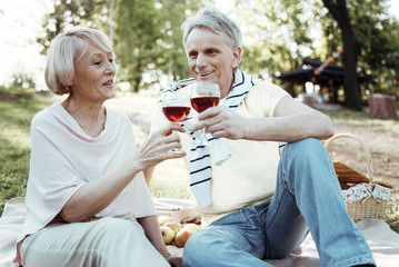 Keep smiling. Cheerful female sitting in semi position and holding glass in right hand while going to drink wine