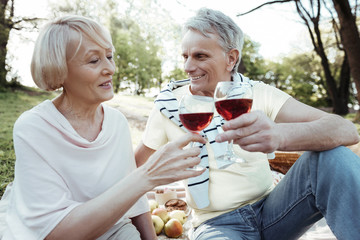 Your favorite. Handsome man holding glass of wine in left hand and keeping smile on face while having romantic picnic with his wife