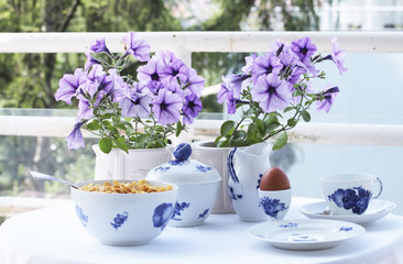 Fototapeta na wymiar Breakfast table set outdoors with purple flowers and white and blue china