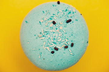 Blue macaron with coconut shavings and chocolate on yellow background
