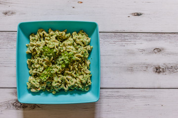Whole grain pasta with spinach and basil on a blue plate on white wooden background