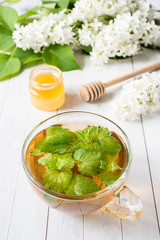 Cup of tea with mint on a wooden table with white lilac flowers