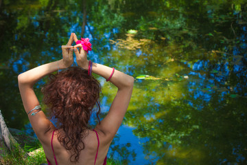 woman practice yoga meditation in front lake hands in mudra gesture with flower in hand back view