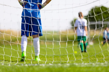 Young Boy as a Football Goalkeeper Standing in a Goal. Football Training Game for Kids. Soccer Players Running After the Ball in the Background. School Outdoor Sport Competitions